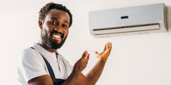 Panoramic Shot Of Happy African American Repairman Smiling At Camera And Pointing With Hands At Air Conditioner